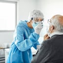 Doctora en traje de protección tomando muestra para la prueba de hisopo del hombre mayor. Un profesional médico está examinando a un paciente anciano durante la crisis de COVID-19. Están en el hospital.
