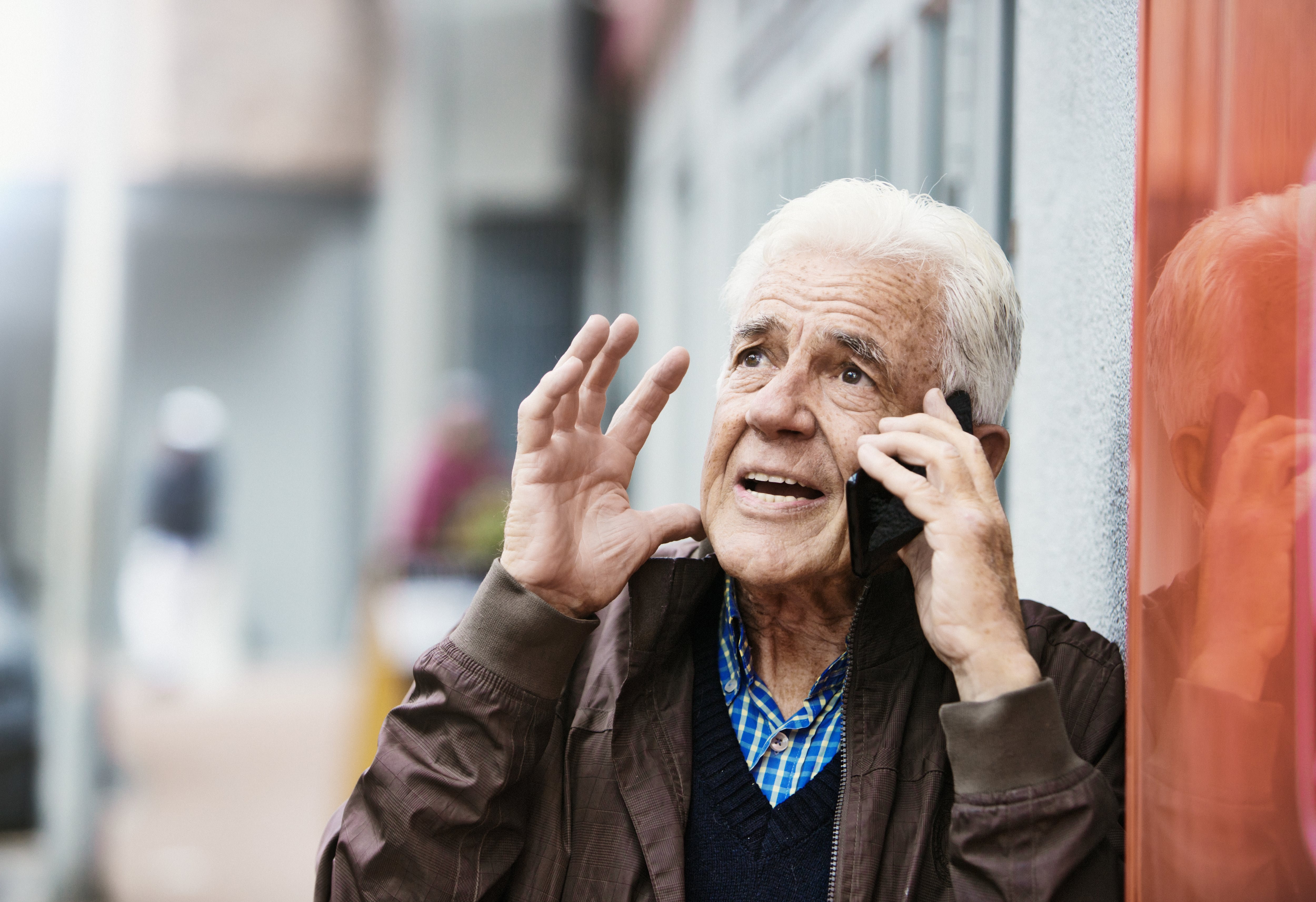 Un hombre mayor que habla por su teléfono móvil en la calle hace un gesto de enojado frustración.