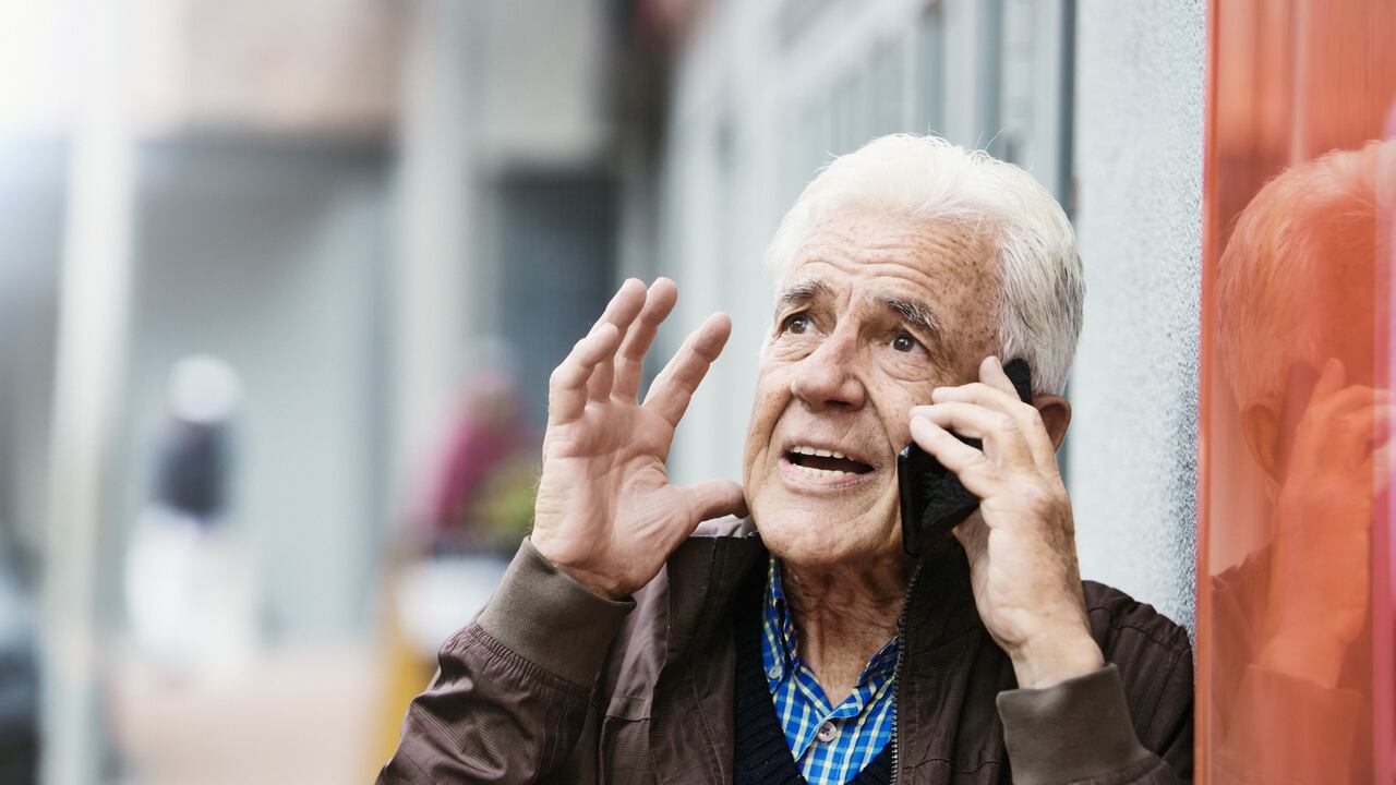 Un hombre mayor que habla por su teléfono móvil en la calle hace un gesto de enojado frustración.