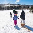 This is a color photograph of a family walking uphill to go sledding in the Colorado Rocky Mountains on a snowy day in winter.