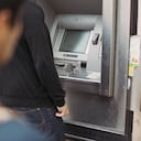 Man using a bank atm machine on the street with a thief watching him from behind