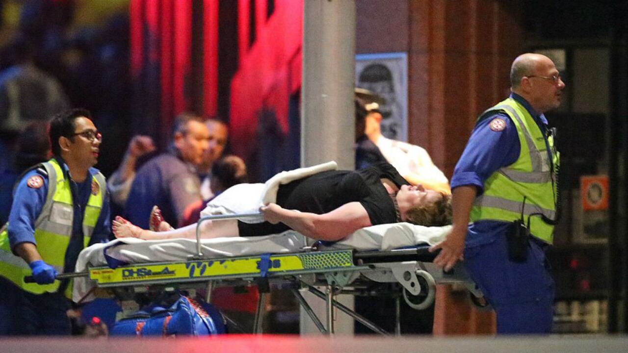 Un rehén herido es trasladado en una camilla por paramédicos, luego de que un policía diera de baja en Sídney a un secuestrador armado que retuvo a 20 personas por 17 horas. (AP)