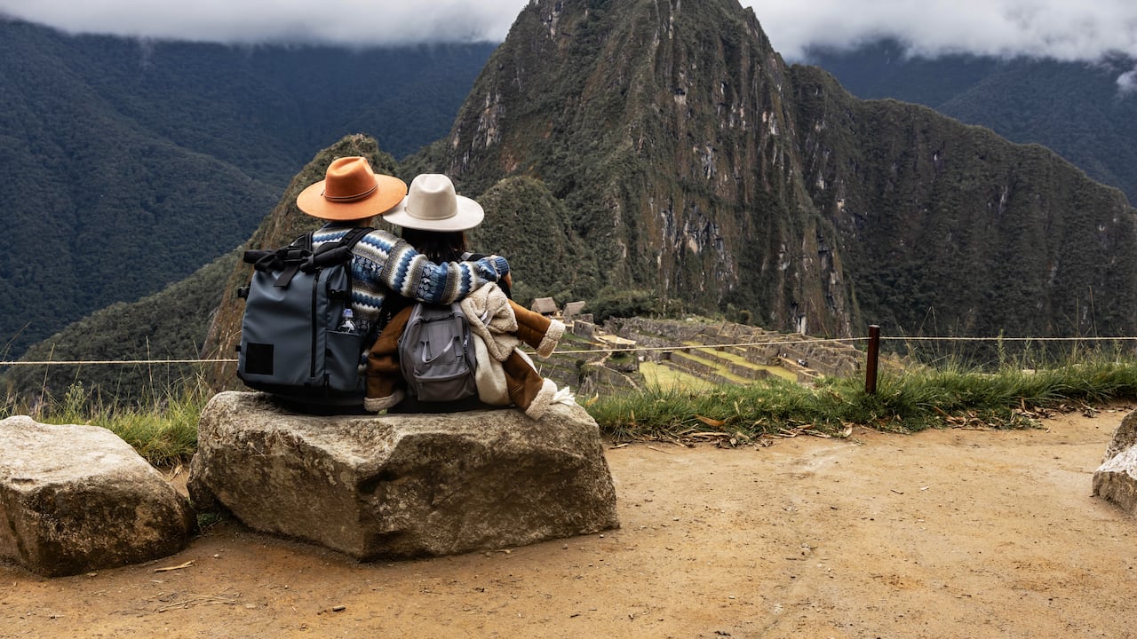 Pareja sentada en una piedra contemplando la impresionante vista de Machu Picchu en Perú.