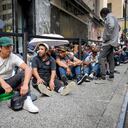 Migrants sit in a queue outside of The Roosevelt Hotel that is being used by the city as temporary housing, Monday, July 31, 2023, in New York. (AP Photo/John Minchillo)