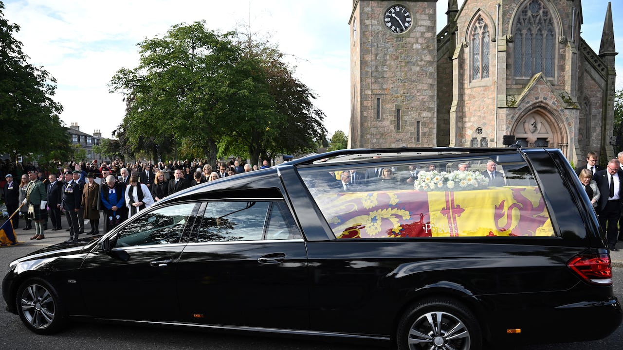 Los miembros del público presentan sus respetos mientras el coche fúnebre que lleva el ataúd de la reina Isabel II, envuelto en el estandarte real de Escocia, pasa por Ballater, el 11 de septiembre de 2022.