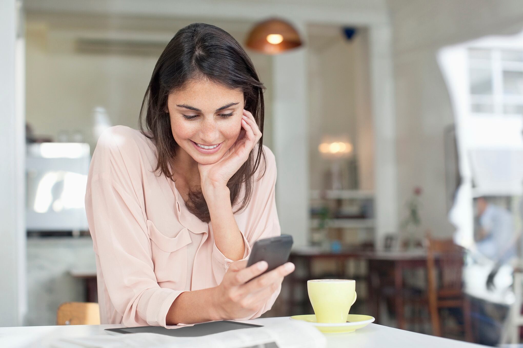 Empresaria sonriente que mira hacia abajo en el teléfono celular en la ventana del café