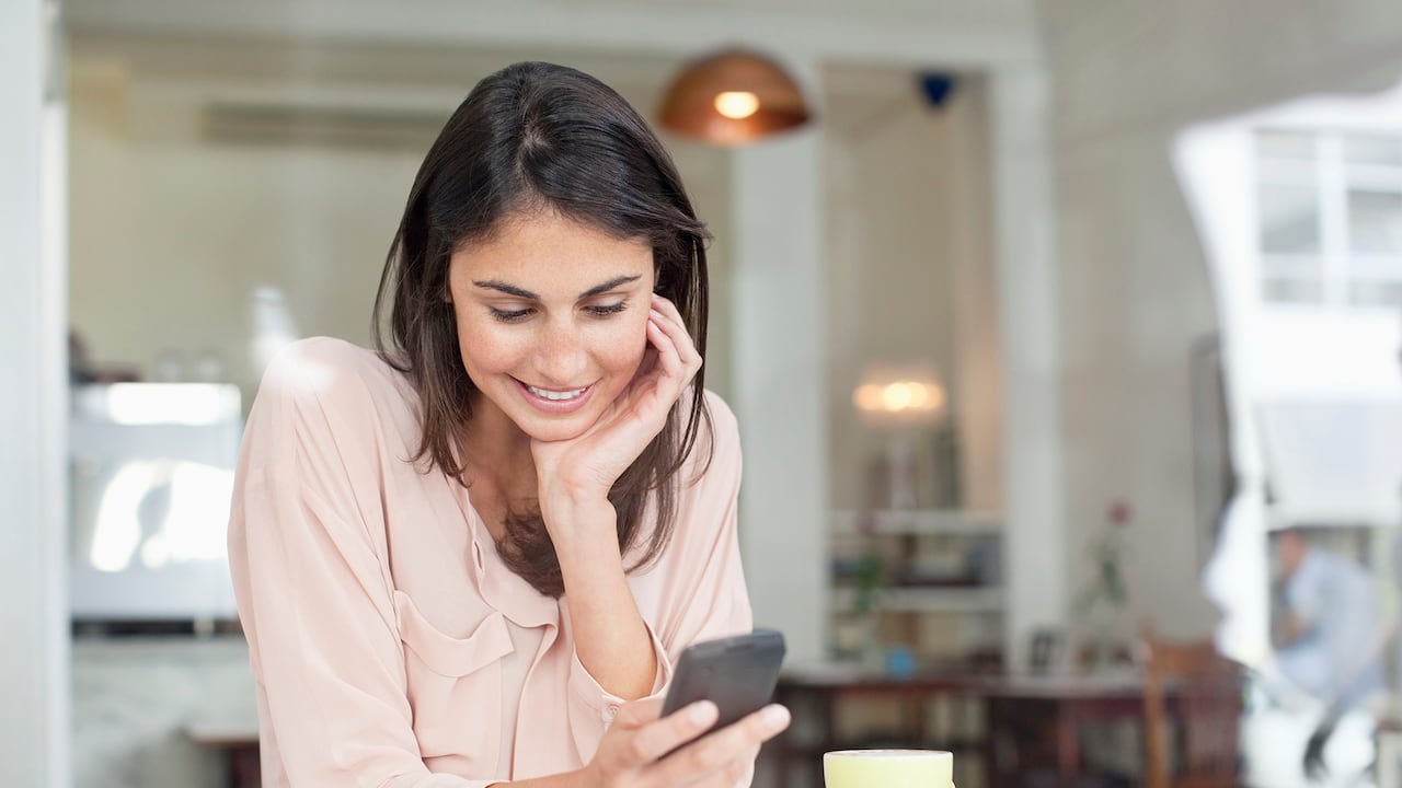 Empresaria sonriente que mira hacia abajo en el teléfono celular en la ventana del café