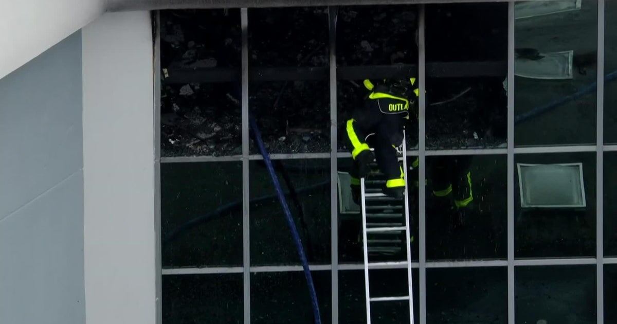 Bomberos rociando agua en un edificio en llamas durante el incendio en Tamarac, mientras el humo cubre la escena.