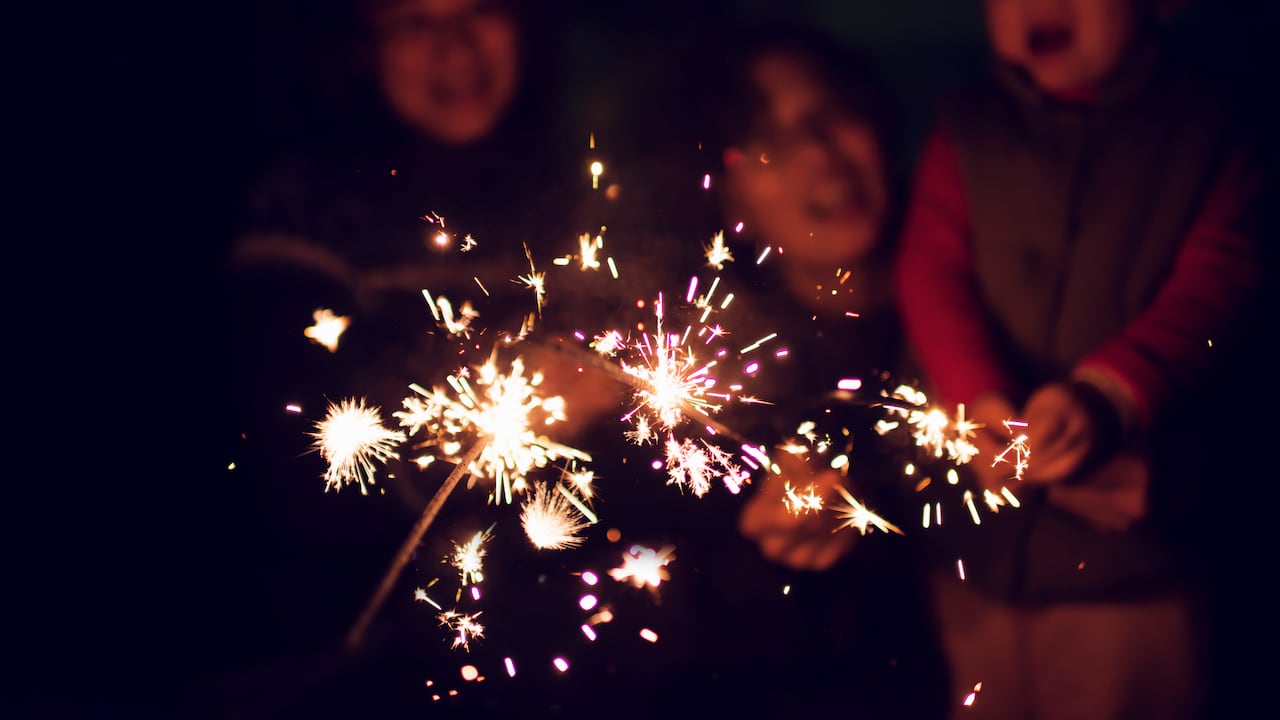 A child is playing sparklers with his family at night