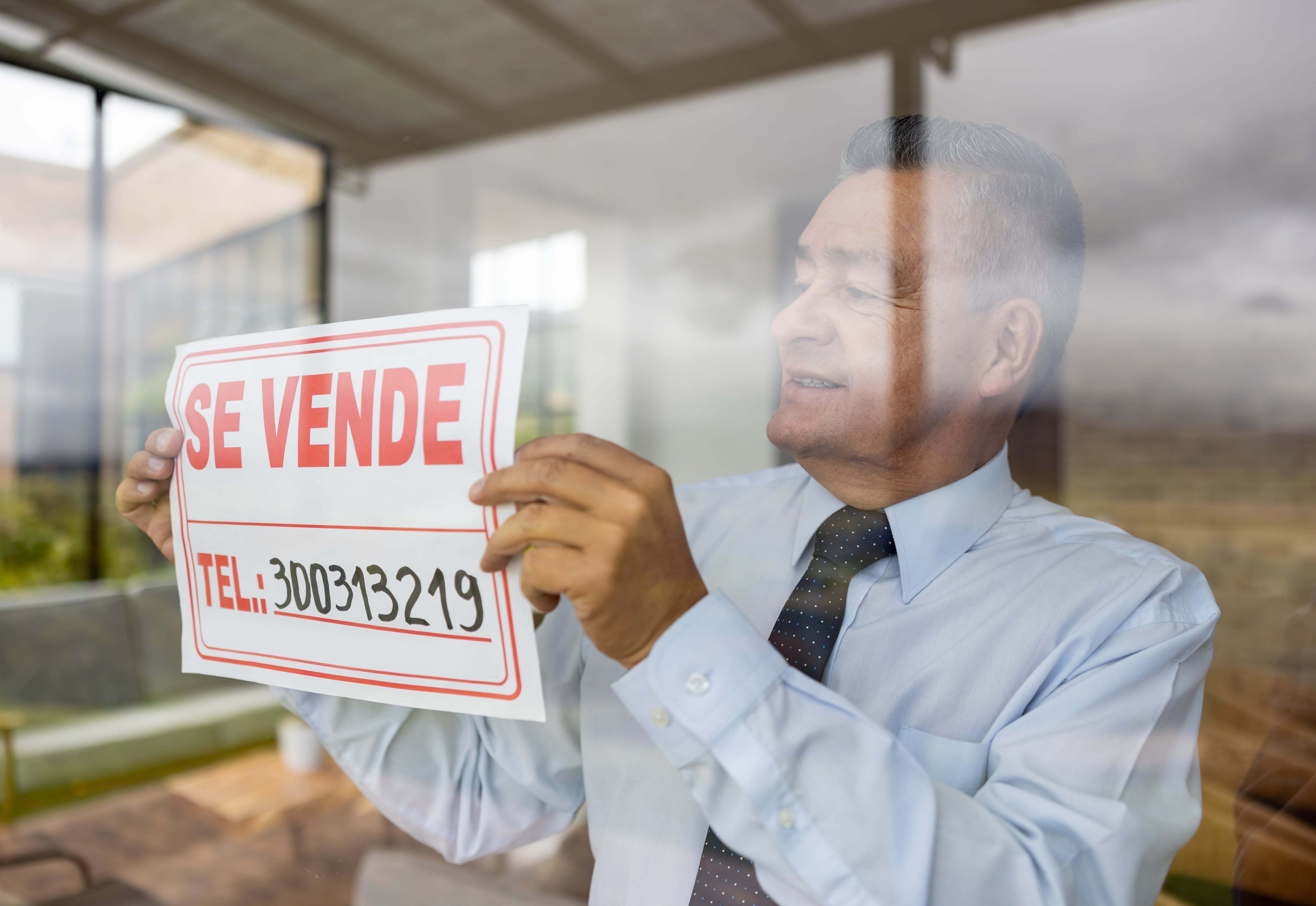 Happy real estate agent hanging a for sale sign on the window of a house