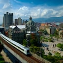 El metro elevado de Medellín está en movimiento mientras se desliza desde la estación de metro Parque Berrio frente a la Plaza Botero. Plaza Botero lleva el nombre del hijo nativo de Medellín y el artista más famoso de Colombia, Fernando Botero. La plaza contiene 23 de sus esculturas más famosas. El Palacio de la Cultura de estilo art nouveau y los edificios de oficinas del centro se pueden ver al fondo.