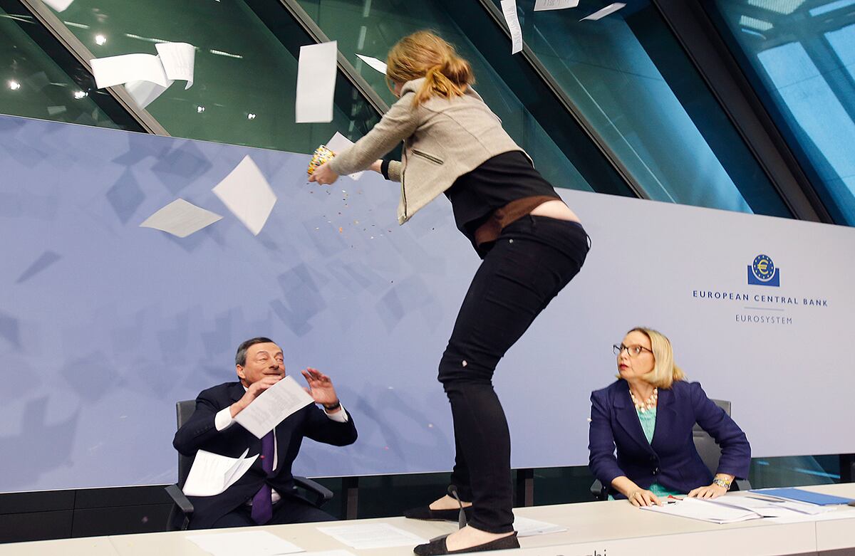 Una activista se para en la mesa para lanzarle papeles al presidente del Banco Central Europeo, Mario Draghi, mientras que la directora de comunicaciones, Christine Graeff, la observa durante una rueda de prensa en Fráncfort, Alemania. (AP)