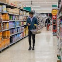 Hombre comprando en un supermercado con un presupuesto ajustado. Está buscando precios bajos debido a la inflación. Vive en el noreste de Inglaterra y utiliza su teléfono móvil para consultar su lista de la compra.