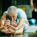 Mature man in seated forward bend pose during yoga class in studio