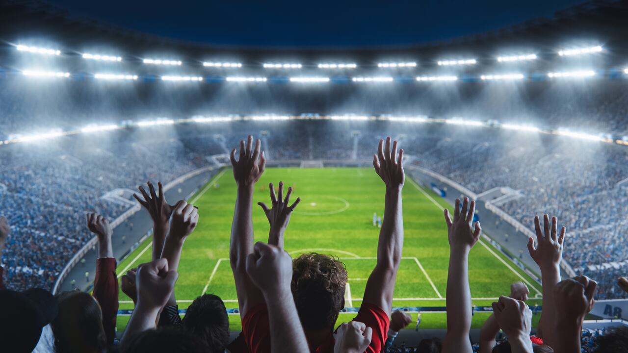High Angle Shot of Fans Cheer for the Team on a Big Stadium During Soccer Championship Match. Teams Play, Crowd of Fans Celebrate Victory. Football Tournament. Wide Angle Of Sold Out National Arena