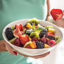 A woman breakfasts a fruit salad high in vitamins and fiber.