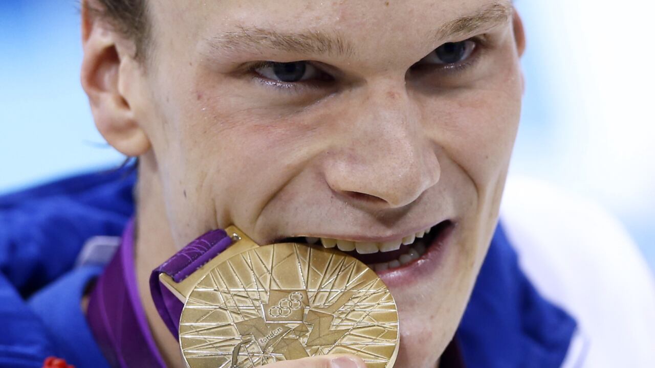 FILE - France's Yannick Agnel bites on his gold medal after winning the men's 200-meter freestyle final at the Aquatics Centre in the Olympic Park during the 2012 Summer Olympics in London, Monday, July 30, 2012. More details have emerged over an investigation into the alleged rape of an underage girl by two-time Olympic swimming champion Yannick Agnel of France, who was arrested last week in Paris. Agnel was handed preliminary charges as part of the investigation after being sent to Mulhouse, eastern France. On Monday Dec.13, 2021, Mulhouse prosecutor said the events allegedly took place in 2016 in several locations including Spain, Thailand and Brazil. (AP/Daniel Ochoa De Olza, File)