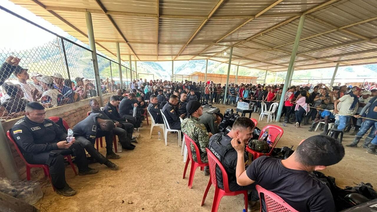 Los uniformados están sentados en sillas mientras que son observados por un gran número de personas.