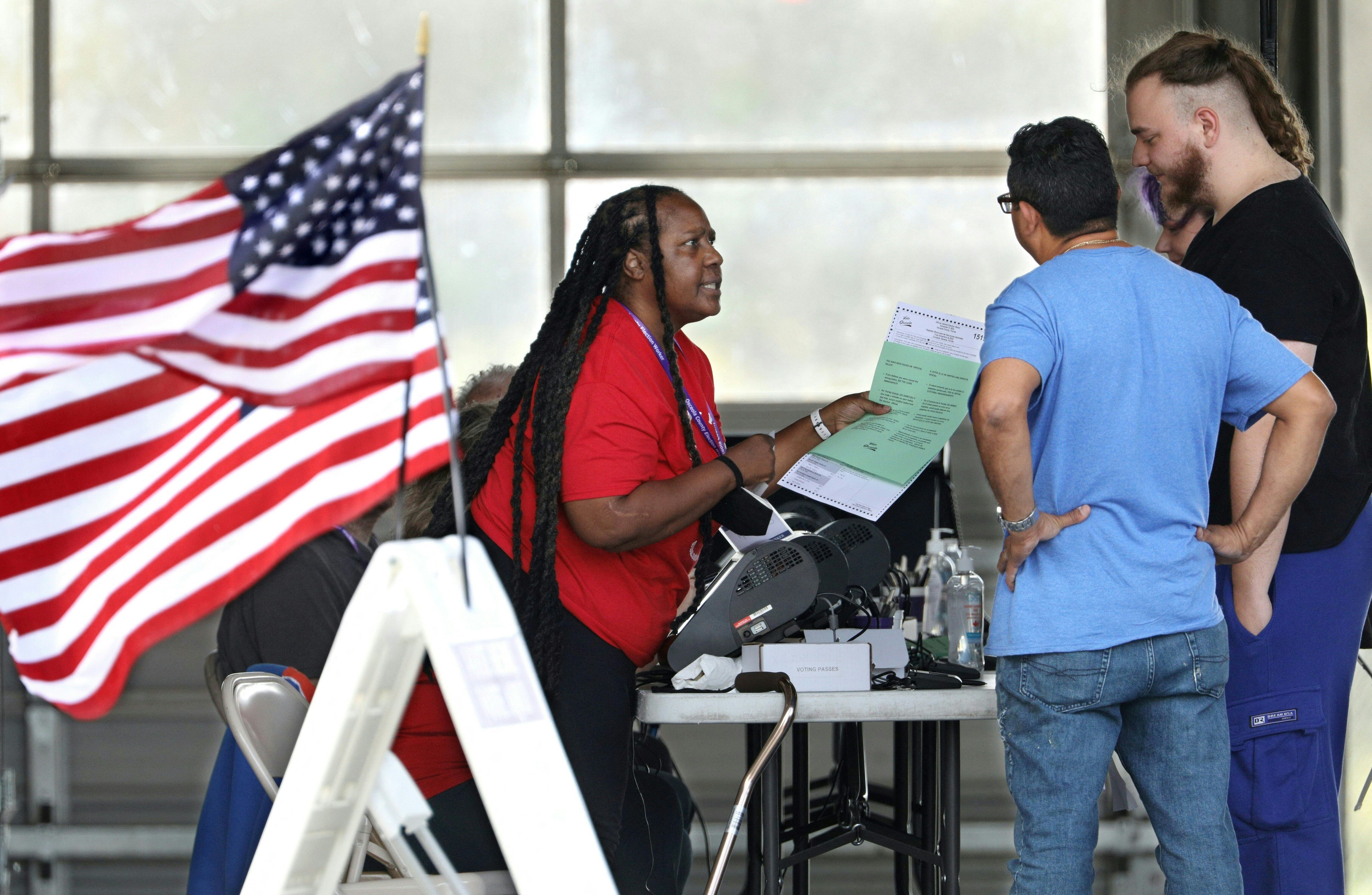 Un funcionario electoral entrega a los votantes boletas con instrucciones sobre cómo votar durante la votación para las elecciones intermedias en un colegio electoral en Kissimmee, Florida, el 8 de noviembre de 2022. (Foto de Gregg Newton / AFP)