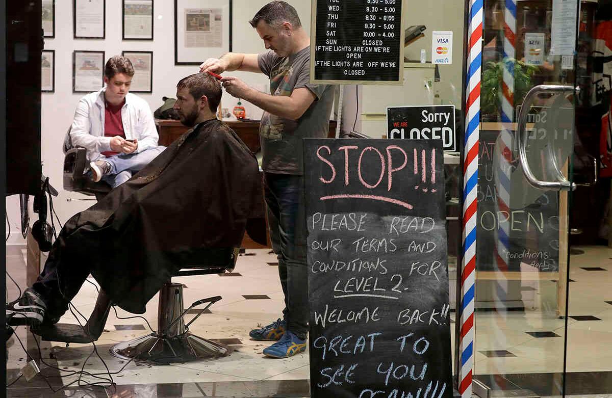 Conrad Fitz-Gerald corta el cabello de un cliente justo pasada la medianoche, en Christchurch, Nueva Zelanda, el 14 de mayo. El país levantó la mayoría de sus restricciones restantes a partir de la medianoche del pasado miércoles. Centros comerciales, tiendas minoristas y restaurantes reabrieron. Foto: Mark Baker/ AP. 