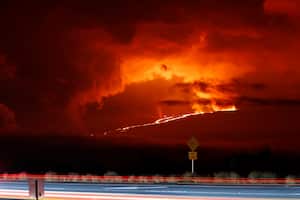 In this long camera exposure, cars drive down Saddle Road as Mauna Loa erupts in the distance, Monday, Nov. 28, 2022, near Hilo, Hawaii. Mauna Loa, the world's largest active volcano erupted Monday for the first time in 38 years. (AP Photo/Marco Garcia)