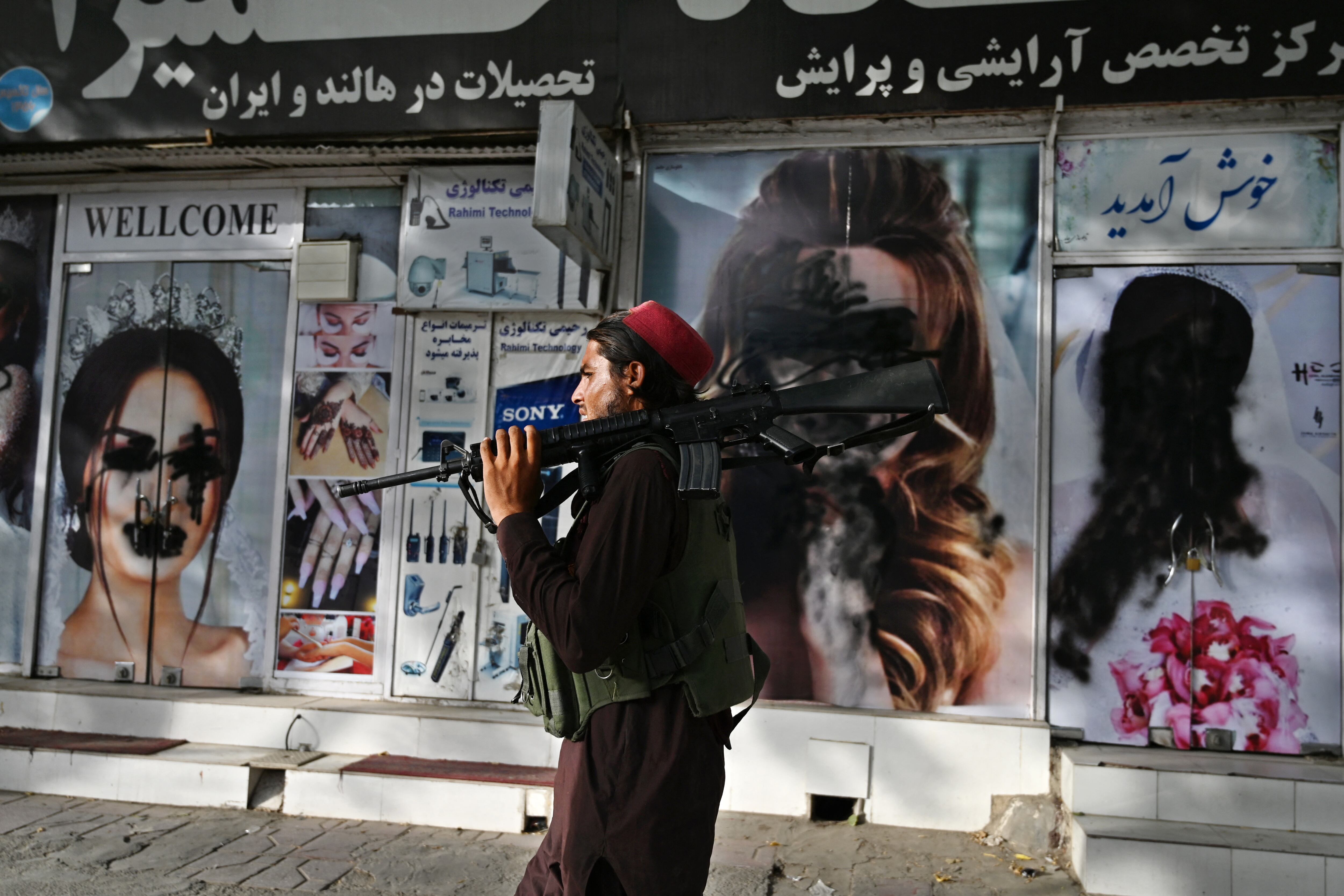 A Taliban fighter walks past a beauty salon with images of women defaced using spray paint in Shar-e-Naw in Kabul on August 18, 2021. (Photo by Wakil KOHSAR / AFP)