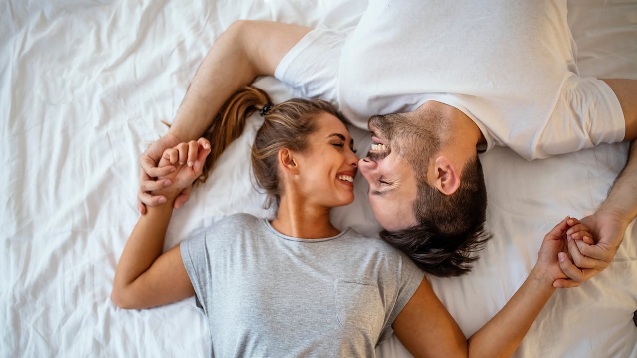 Chico y chica en un acogedor ambiente hogareño. Hombre y mujer felices acostados en la foto de stock del dormitorio. Vista superior de una pareja joven sonriente abrazándose en la cama por la mañana. Hermoso par de amantes abrazo y beso