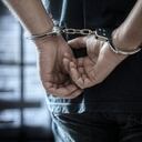 Arrested man in handcuffs with handcuffed hands behind back in prison