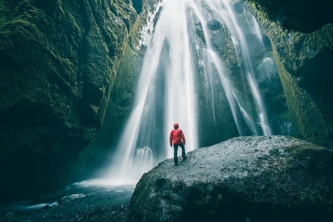 Tourist on a rock admiring Gljufrabui waterfall, Iceland