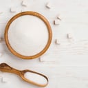 Azúcar blanco en un tazón y cuchara sobre fondo de mesa de madera