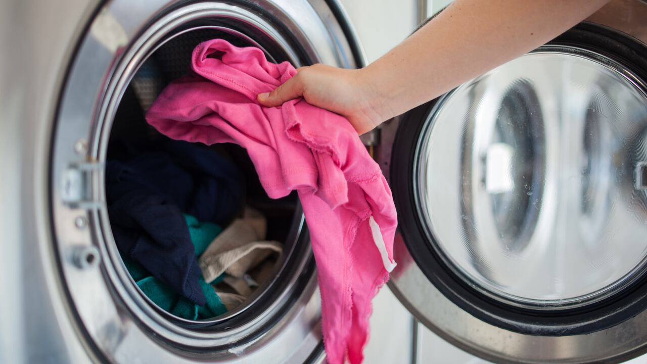 Woman putting pink shirt into washing machine.