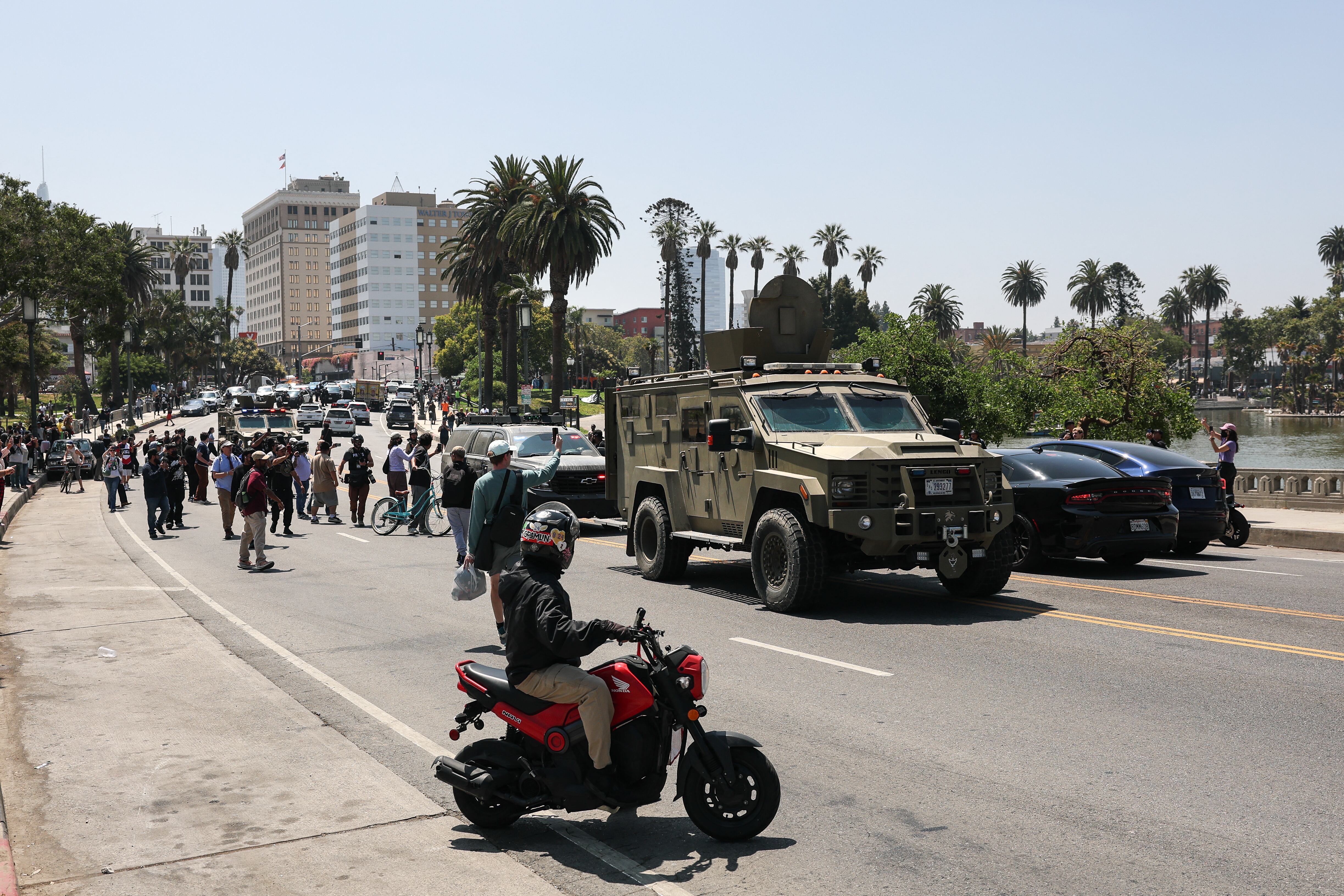 Onlookers watch as federal agents with US Customs and Border Patrol (CBP) ride in multiple armored vehicles driving slowly down Wilshire Boulevard near MacArthur Park in Los Angeles, California, on July 7, 2025. (Photo by Patrick T. Fallon / AFP)