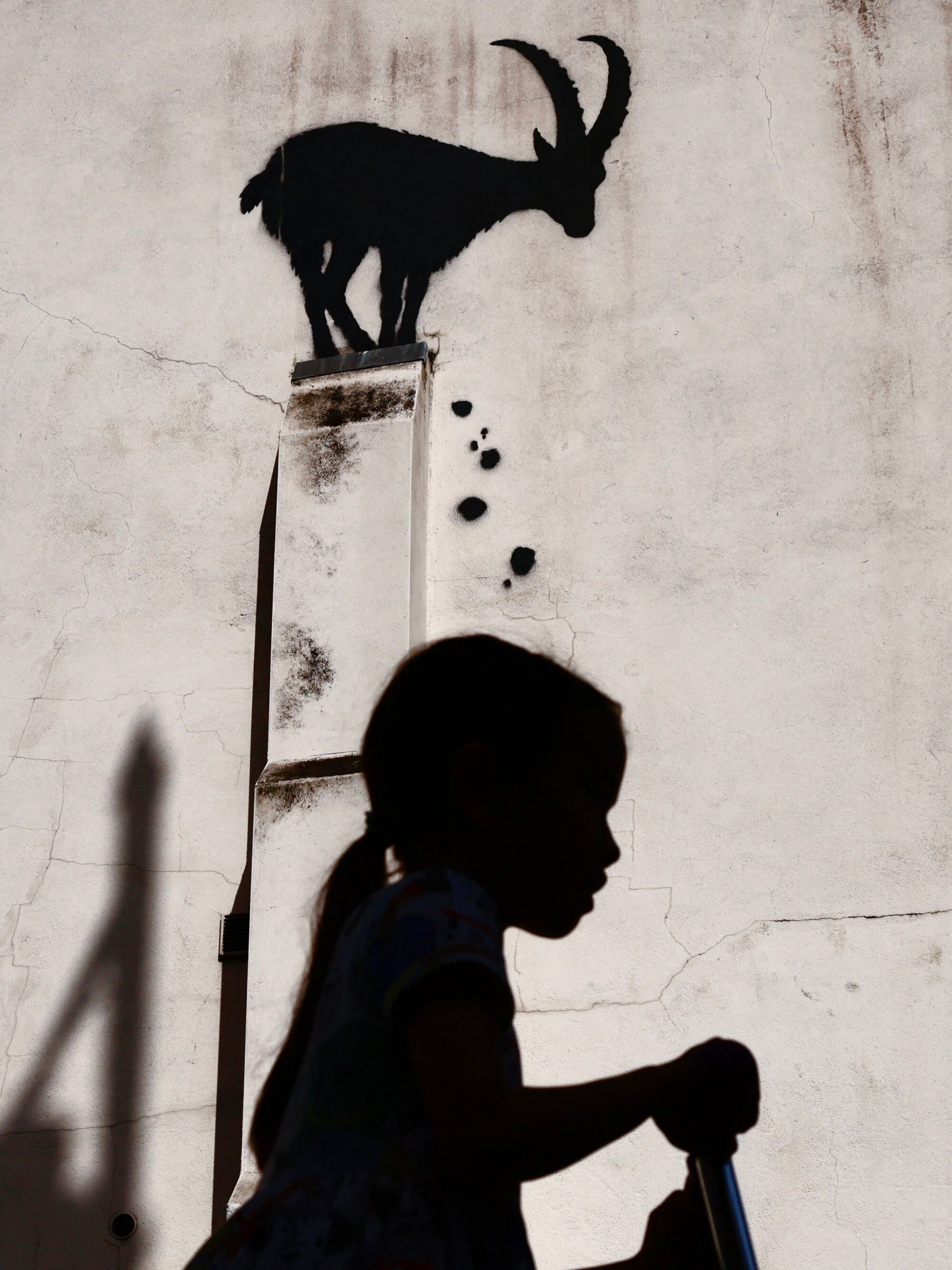 A photograph taken on August 5, 2024 shows a child riding a scooter past a stencilled Banksy artwork, depicting a mountain goat and falling rubble at the top of a pillar, on the side of a building in Kew Gardens, west London. The Artist confirmed the work to be theirs after posting an image of it on the social media app Instagram. (Photo by BENJAMIN CREMEL / AFP) / RESTRICTED TO EDITORIAL USE - MANDATORY MENTION OF THE ARTIST UPON PUBLICATION - TO ILLUSTRATE THE EVENT AS SPECIFIED IN THE CAPTION
