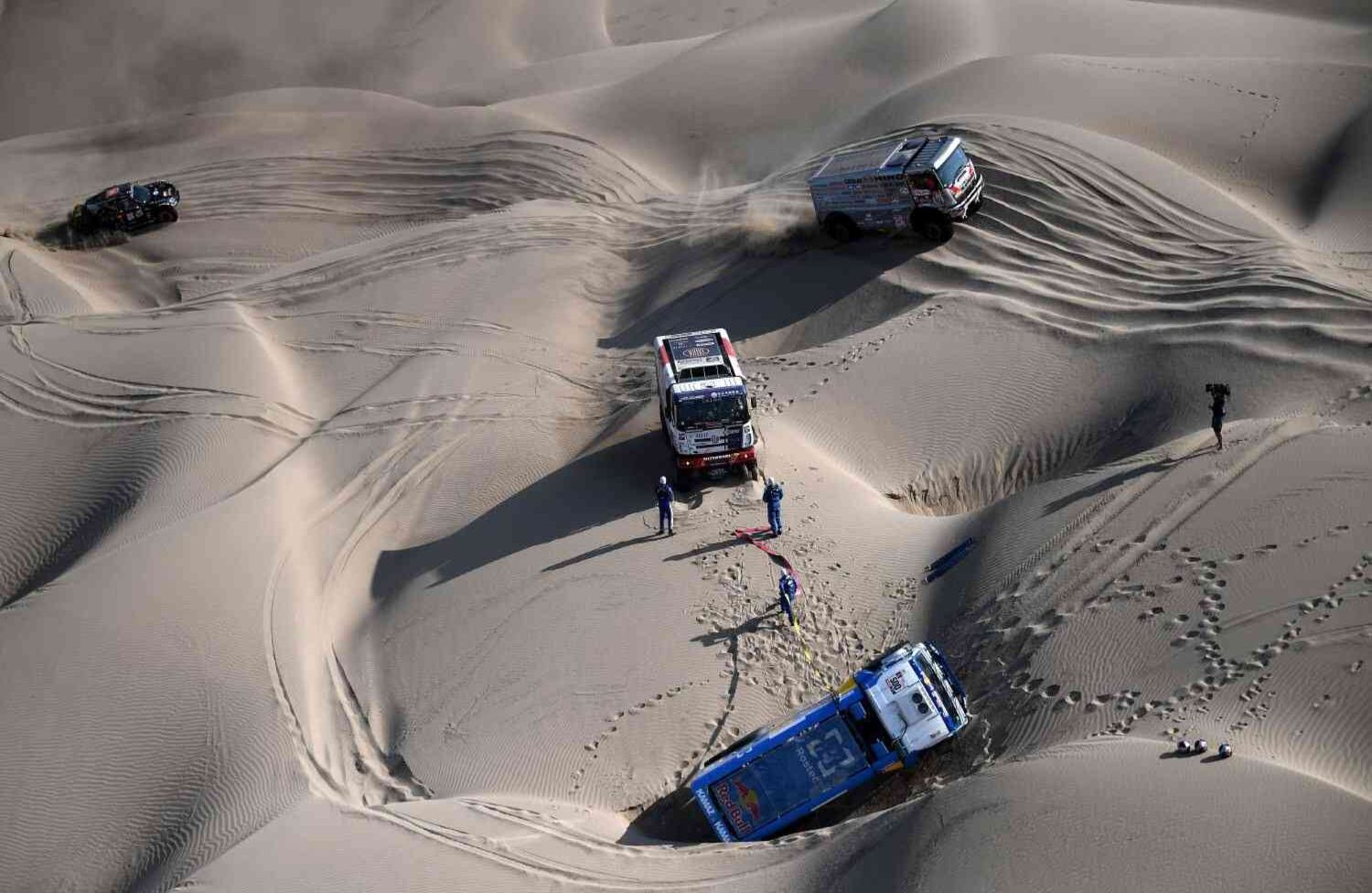 El camionero checo Martin Kolomy de Tatra, su copiloto Jiri Stross y el mecánico Rostislav Plny (C) ayudan al piloto ruso Kamaz Eduard Nikolaev, a los copilotos Evgeny Yakovlev y al mecánico Vladimir Rybakov después de que su camión se volcó durante la etapa 5 entre San Juan de Marcona y Arequipa en Perú, el 10 de enero de 2018. / AFP PHOTO / Franck FIFE.