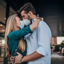 Una joven pareja con tapabocas y besándose al aire libre en la ciudad.