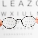 Optometrista poniendo anteojos al paciente después del examen de la carta optométrica