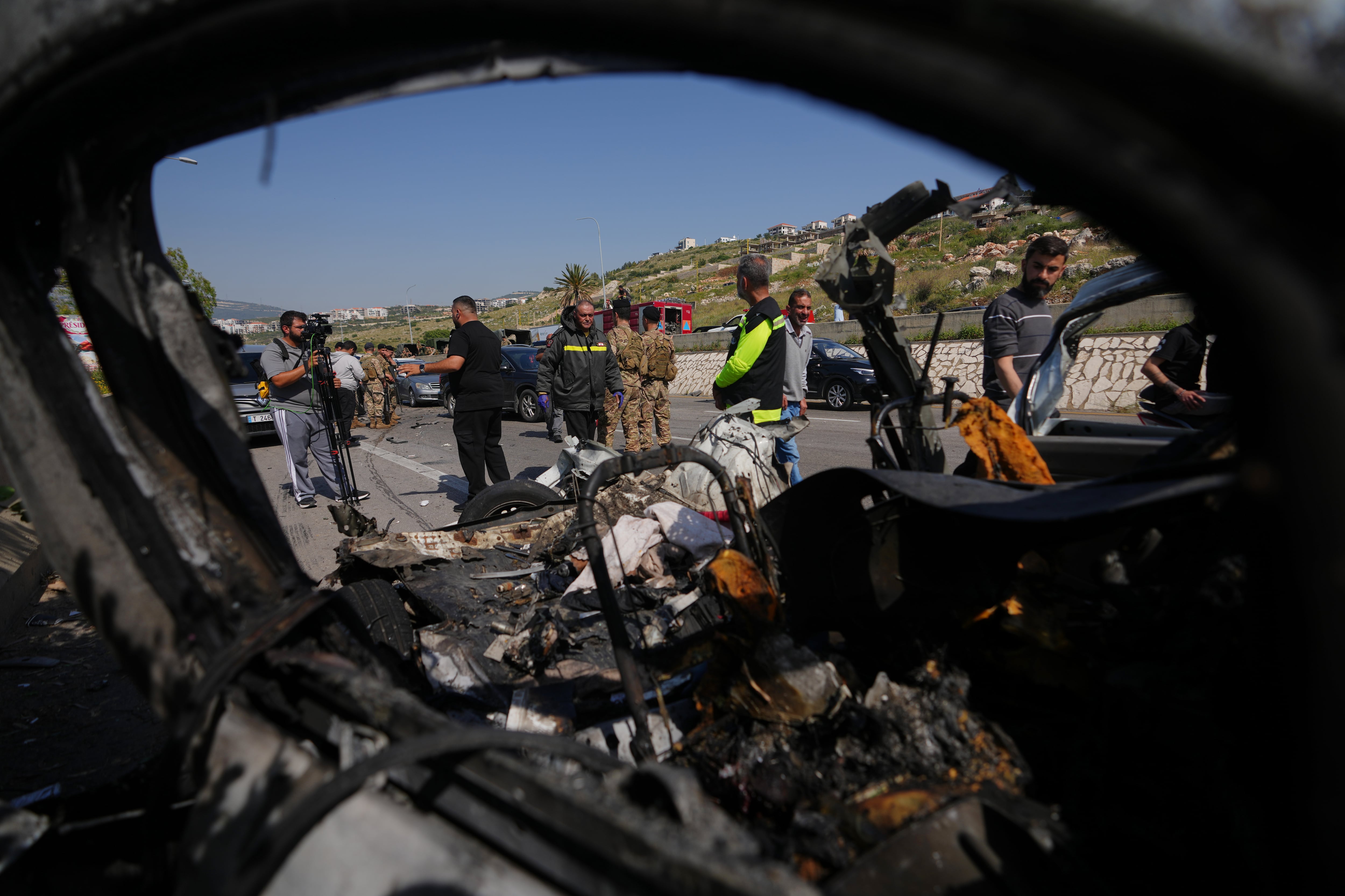 Varias personas inspeccionan los restos calcinados de un vehículo en el lugar donde un ataque aéreo israelí impactó un automóvil en la ciudad costera de Saadiyat, al sur de Beirut, Líbano.