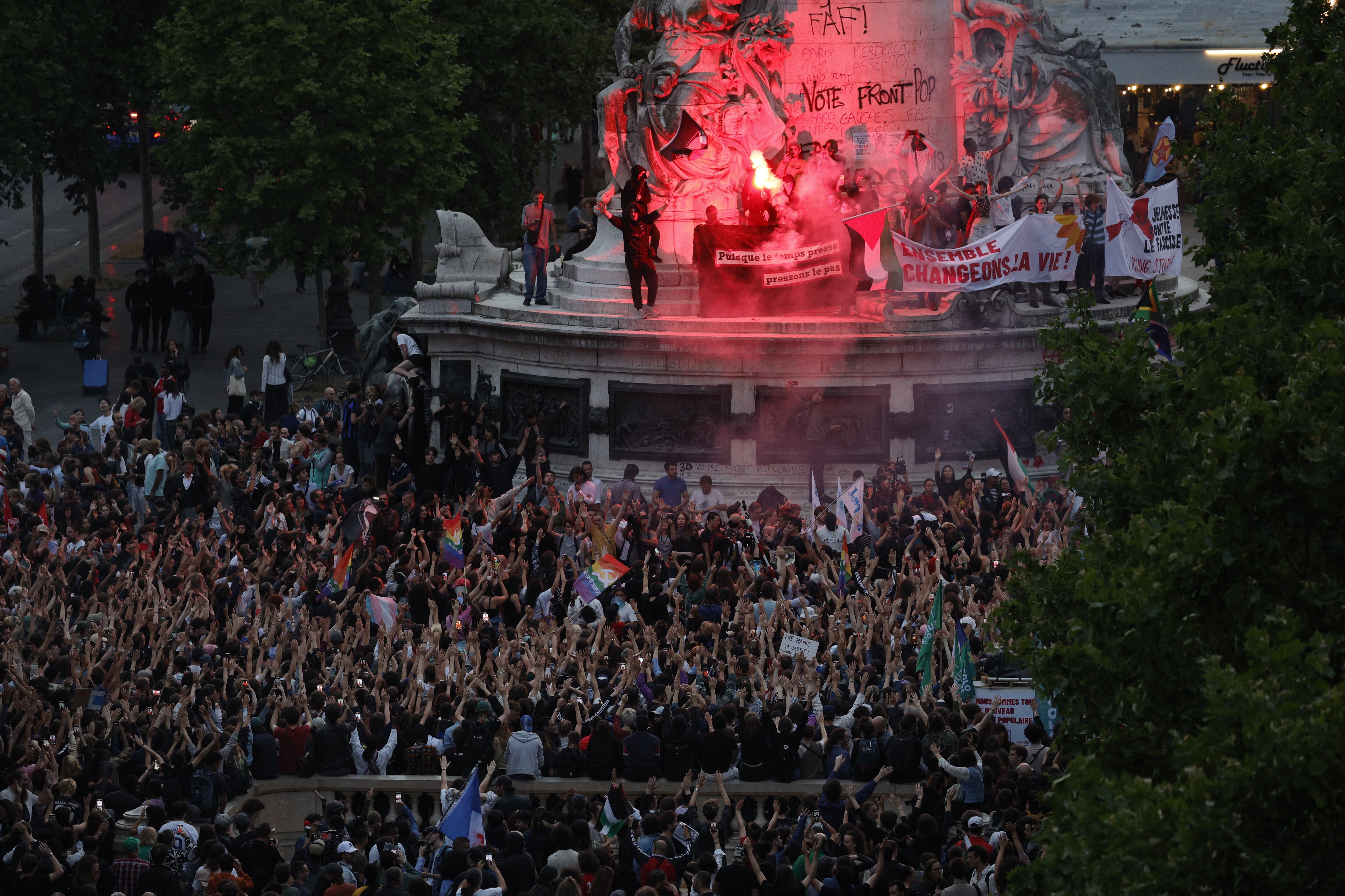 Los manifestantes que se encuentran en el Monumento a la República encienden bengalas mientras participan en una manifestación después del anuncio de los resultados de la primera vuelta de las elecciones parlamentarias francesas, en la Place de la Republique en París el 30 de junio de 2024. Habiendo salido claramente En cabeza en la primera vuelta de las elecciones legislativas, la Asamblea Nacional (RN) y sus aliados podrían obtener una amplia mayoría relativa en la Asamblea Nacional, o incluso una mayoría absoluta, según las proyecciones de tres institutos electorales, que predicen entre 240 y 310 asientos.