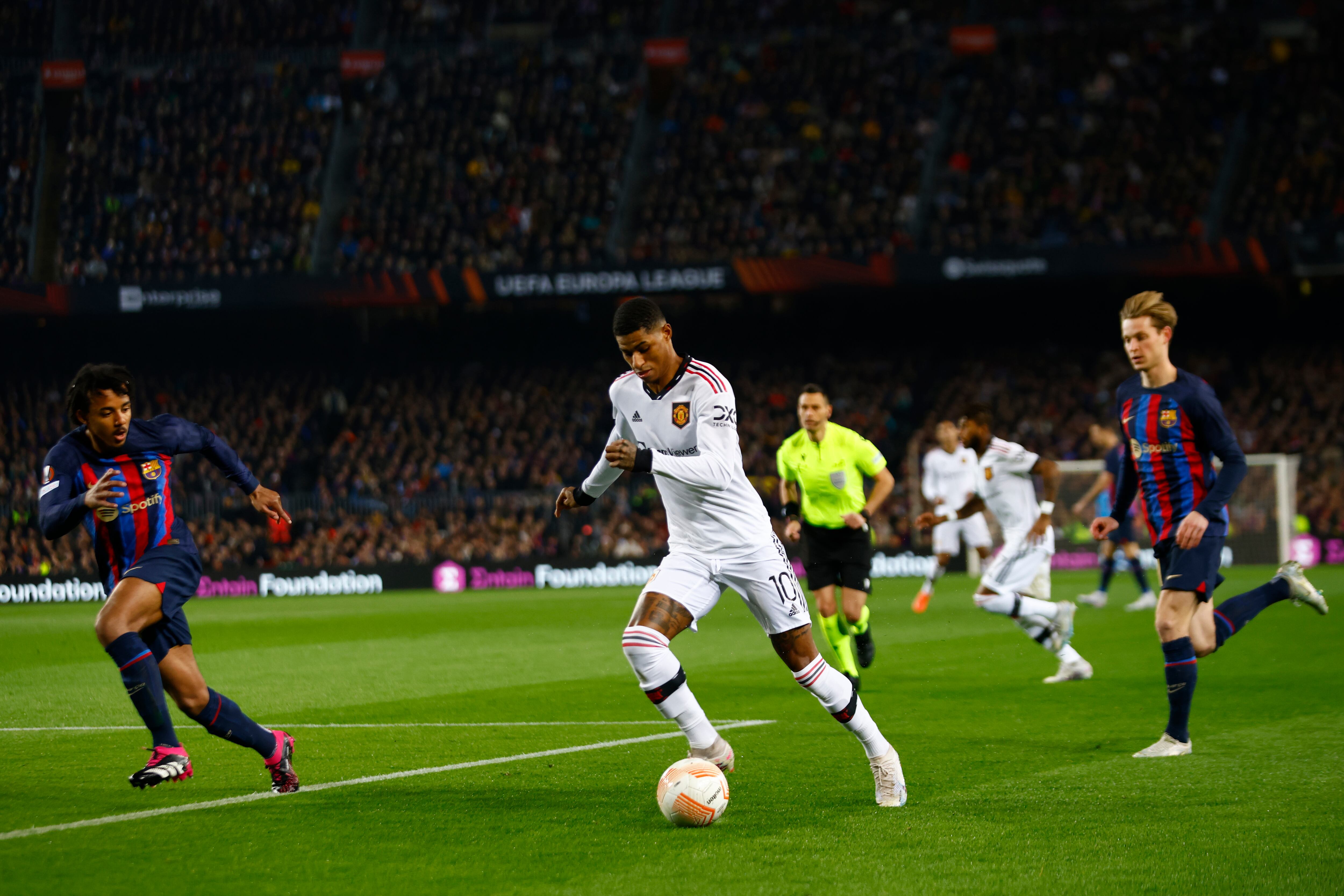 Manchester United's Marcus Rashford, centre, runs with the ball between Barcelona's Jules Kounde, left, and Barcelona's Frenkie de Jong during the Europa League playoff first leg soccer match between Barcelona and Manchester United at the Camp Nou stadium in Barcelona, Spain, Thursday, Feb. 16, 2023. (AP Photo/Joan Monfo