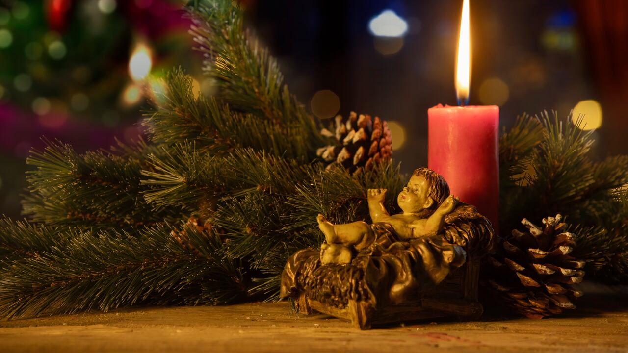 Ramitas de abeto con una estatua del Niño Jesús y una vela encendida sobre un fondo de árbol de Navidad borroso