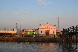 Un grupo de jóvenes juega fútbol en una cancha de tierra frente a la iglesia en Nueva Venecia.
