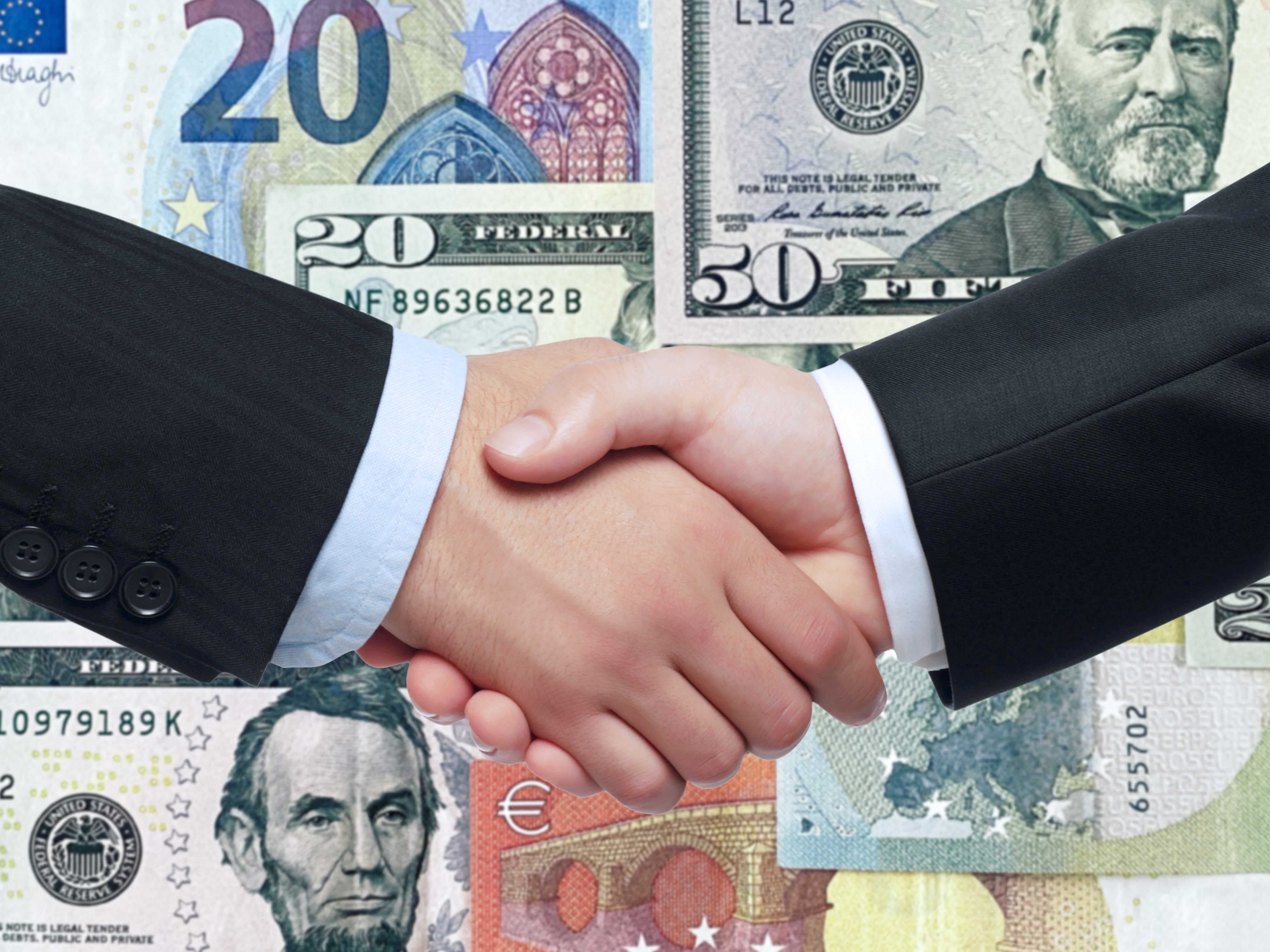 Close up shot of businessman handshaking in front of dollar bills