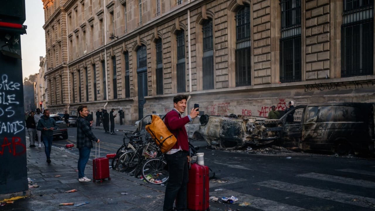 Un turista utiliza su teléfono inteligente para grabar vehículos calcinados durante una jornada de protestas contra el «alto costo de la vida» en París, el 17 de octubre de 2026