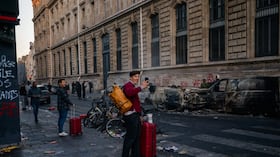 Un turista utiliza su teléfono inteligente para grabar vehículos calcinados durante una jornada de protestas contra el «alto costo de la vida» en París, el 17 de octubre de 2026