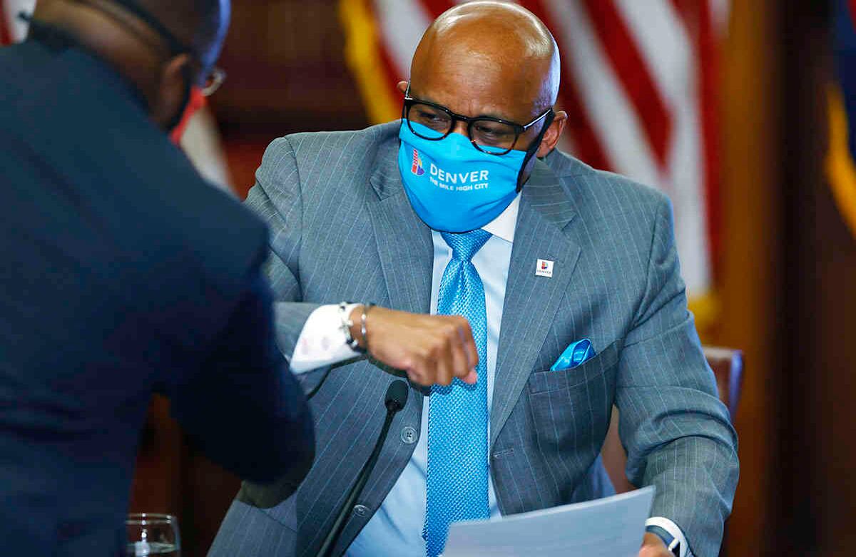 El alcalde de Denver, Michael Hancock, de regreso, usa una máscara facial mientras saluda a un funcionario de la ciudad después de una conferencia de prensa para explicar el plan de la ciudad para permitir que las empresas se reabran a medida que la ciudad permanece la orden de estar  en el hogar. (Foto AP / David Zalubowski)