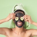 Happy smiling girl applying facial carbon mask portrait - Young woman having skin care cleanser spa day - Healthy beauty clean treatment and and self care lifestyle concept - Green background