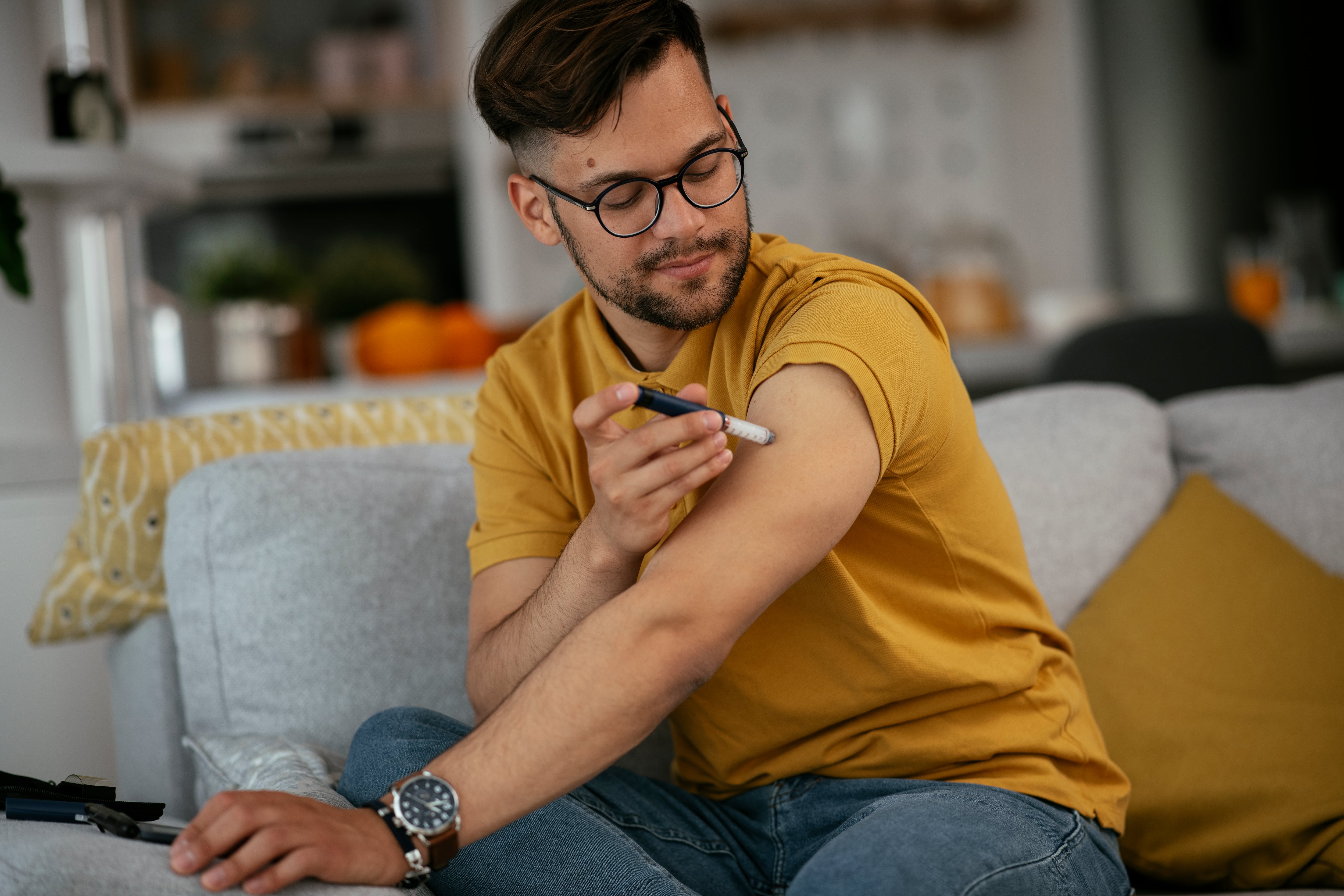 Young man giving himself an insulin shot at home.