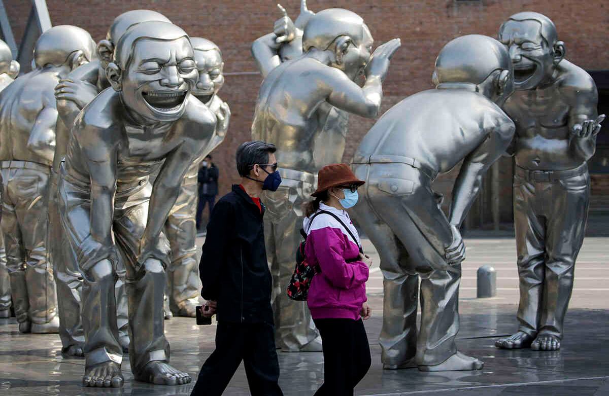 Las personas caminan por esculturas humanas en exhibición afuera de una galería de arte en Beijing, usando tapabocas. Andy Wong / AP