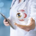 Doctor en mano muestra ojo sobre fondo borroso.