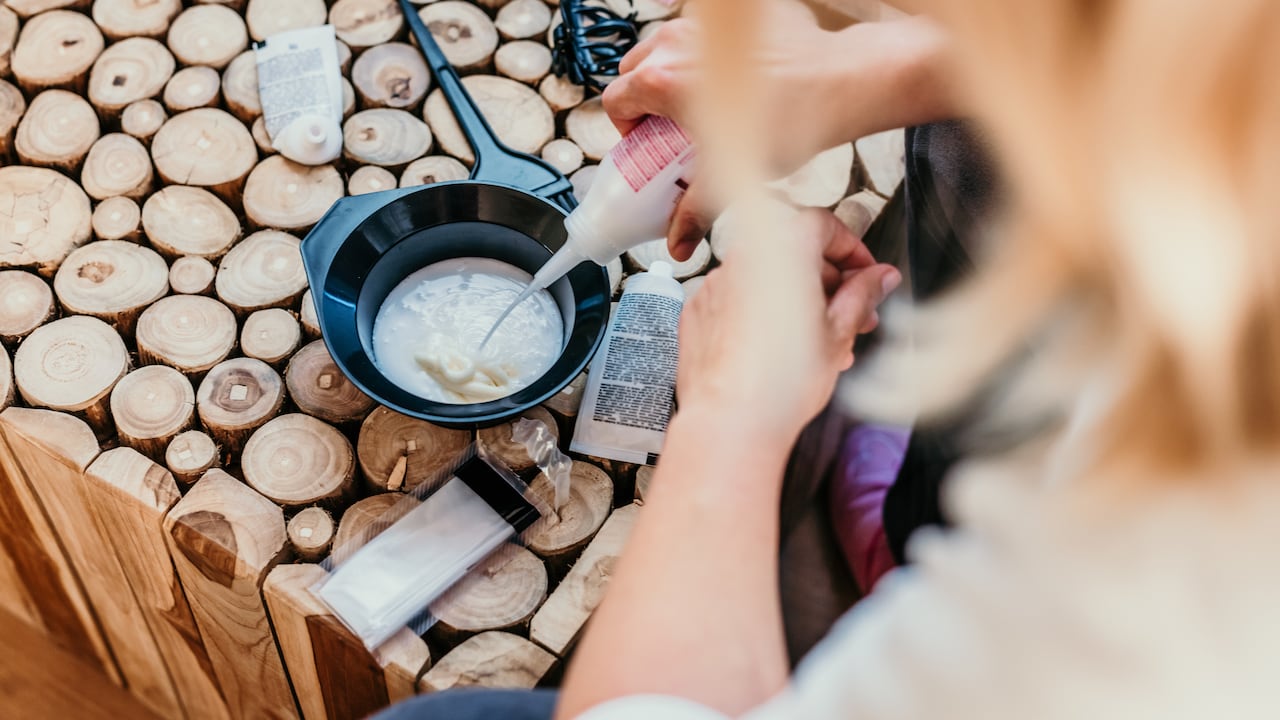 Mano de mujer vertiendo tinte para el cabello mezcla de ingredientes en un tazón